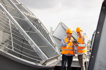 Asian engineer refrigeration plant  factory. male mechanic wearing helmet and Reflective Safety Vest uses laptop, tablet, equipment with sets of cooling towers conditioning systems background.