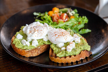 Two avocado toasts with poached eggs and fresh salad on the side, healthy delicious breakfast