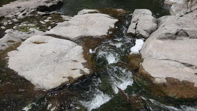 Selective focus close-up of clear stream water running over large rocks. Water running through a parkland during the daytime. Water runs through the stones summer time
