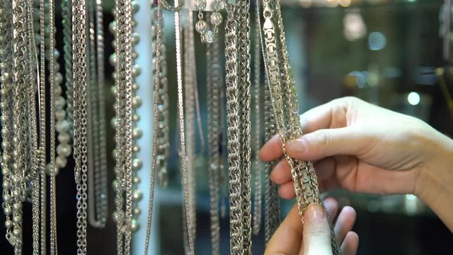Women's hand picks silver and gold chains to buy. Women choosing bijouterie in the store.