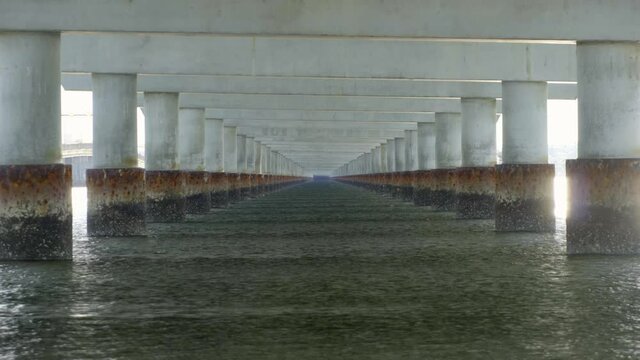 Rows of pylons in water under very long straight bridge, looping fixed shot
