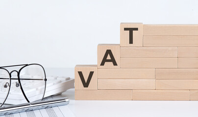 wooden cubes with letters VAT on the white table with keyboard and glasses