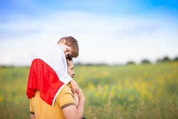 Dad with his little son on his shoulders walking in the field covered with flag of Poland. Father's day in Poland. Polish Flag Day. Independence Day. Love Poland, travel concept. Selective focus.