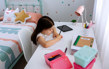 Girl doing homework sitting at a desk in her bedroom