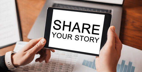 Man hands holding tablet with text Share your story at workplace. Businessman working at desk with documents