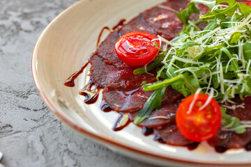 Beef carpaccio with arugula and parmesan on gray surface
