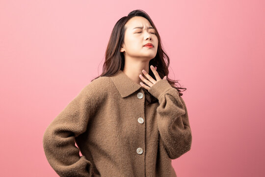 Oriental beauty with sore throat on pink background