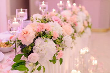 Luxurious decoration of wedding table with flower garlands and burning candles. Wedding floristry. Concept of wedding events. Beauty and luxury.