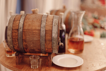 Wooden barrel lined with brass rings lies on display table. Next to it is plate and glass glasses. Strong alcoholic beverages. National traditions. Culture of winemaking.