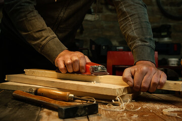 Carpenter is using sandpaper on a piece of wood in workshop. Sanding wooden plank.	