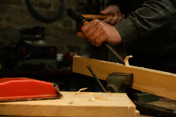 Carpenter chiselling wooden plank in the workshop.	