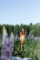 portrait of a sexy girl in a straw hat. A fashionable Caucasian woman feels free in a field with purple flowers in the sun. Lupine field in summer. The concept of a summer countryside. Perfect  body. 