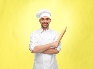 cooking, culinary and people concept - happy smiling male chef or baker in toque with rolling pin over illuminating yellow background