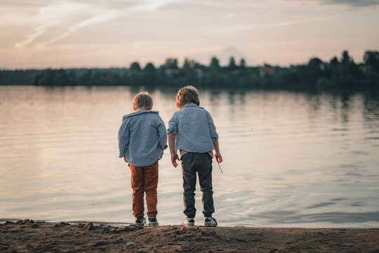 Two brothers stand on the shore of a lake or river at sunset.