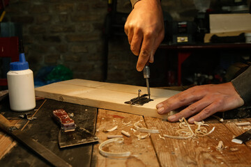 Carpenter screwing metal chrome hinges on wooden plank in the workshop.	
