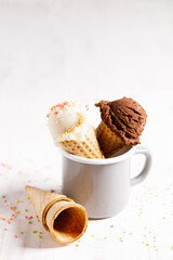 Ice cream scoops in cones on white wooden background.