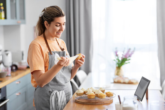 culinary, bake and cooking food concept - happy smiling young woman with baking bag making cupcake topping on kitchen at home