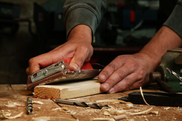 Fototapeta na wymiar Carpenter is using sandpaper on a piece of wood in workshop. Sanding wooden plank. 