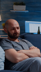 Fototapeta premium Stressed depressed traumatised, frustrated man looking in distance, sitting alone on sofa feeling emotionally unstable, lonely desperate, vulnerable suffering from anxiety, chronic disease