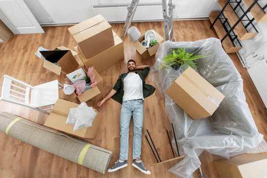 moving, people and real estate concept - happy smiling man with boxes lying on floor at new home