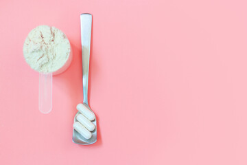 Protein scoop and capsules on pink background close up, copy space