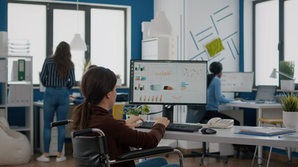 Paralysed financial expert sitting in wheelchair analysing economy statistics of company in business office typing on computer. Handicapped, immobilized businesswoman using modern technology.