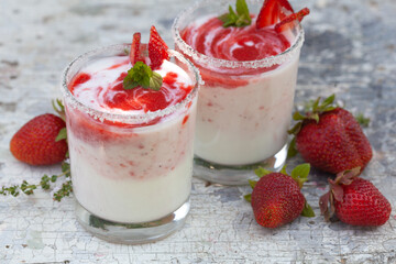 Two glasses of yogurt with strawberries on the table.