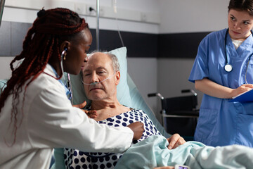 African american cardiologist checking examining senior patient heart, using stethoscope while...