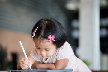 Cute little Asian girl drawing on tablet indoor. 