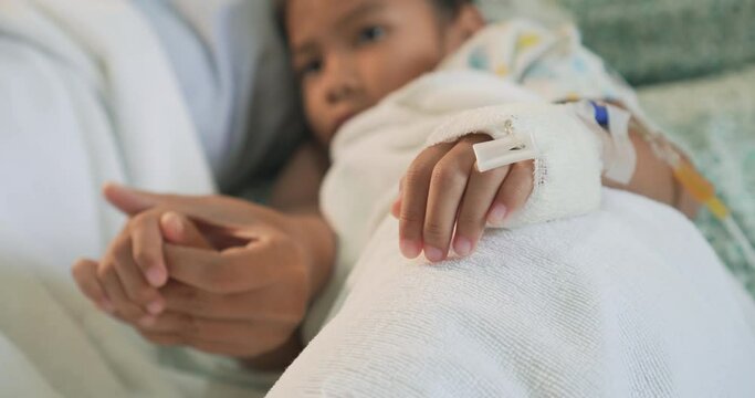 Mother is holding hand bandaged of daughter in hospital bed sleeping