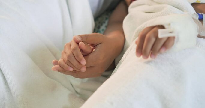 Mother is holding hand bandaged of daughter in hospital bed sleeping