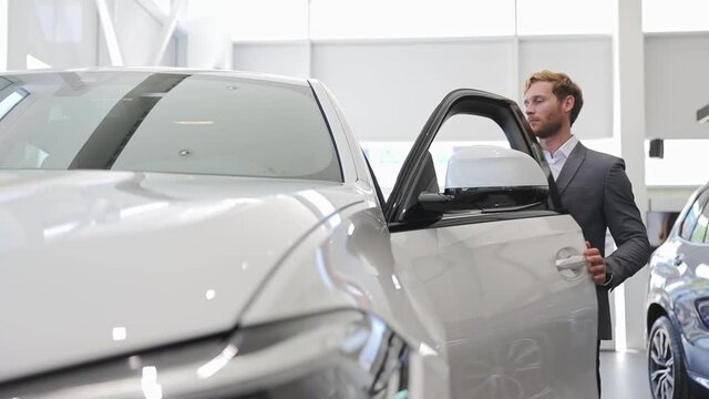 Happy adult man customer male buyer businessman client wears classic suit chooses auto wants to buy new automobile in car showroom vehicle salon dealership store motor show indoors. Car sales concept