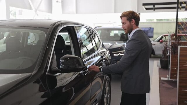 Man customer male buyer client wears classic suit chooses auto wants to buy new automobile in car showroom vehicle salon dealership store motor show push button key open door sit indoor. Sales concept