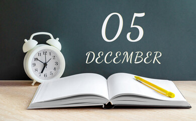 december 05. 05-th day of the month, calendar date.A white alarm clock, an open notebook with blank pages, and a yellow pencil lie on the table.Winter month, day of the year concept