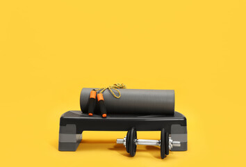 Step platform, dumbbell, mat and jump rope on yellow background. Sports equipment