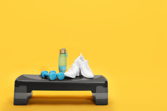 Step platform, dumbbells, shoes and bottle of water on yellow background. Sports equipment