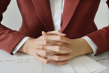 Close up photo of businesswoman in burgundy suit, crossing hand on a table with paper works.