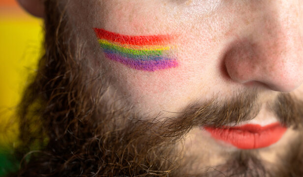 Young handsome bearded man with pride flag on his cheek, rainbow flag standing for LGBTQ, Gender right and sexual minority. Portrait