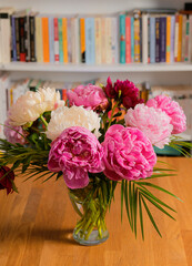 Flowers and books. Beautiful view of a bouquet of red rose peonies ia vase on a wooden table with a lot of books in background.