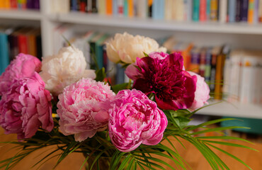 Flowers and books. Beautiful view of a bouquet of red rose peonies ia vase on a wooden table with a lot of books in background.