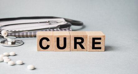 CURE inscription on wooden cubes isolated on white background, medicine concept. Nearby on the table are a stethoscope and pills.