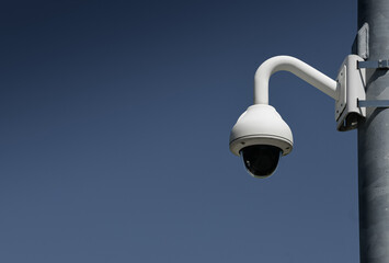 Building security. A white surveillance camera on a pole against a blue sky background.