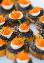 A lot of small pieces of bread with red and black caviar. Delicious catering food.