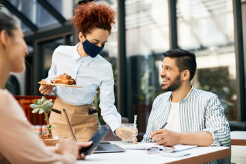 Waitress with protective face mask and gloves serving guests in a cafe.
