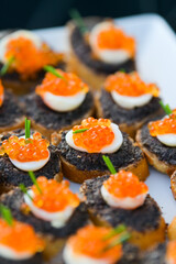 A lot of small pieces of bread with red and black caviar. Delicious catering food.