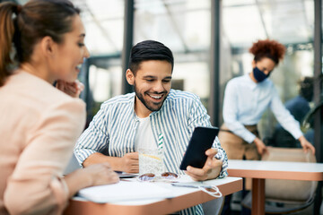 Happy man and his girlfriend using smartphone while relaxing at reopened cafe during COVID-19 pandemic.