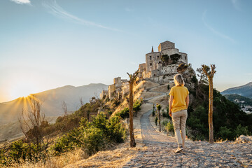 Athmosphere of beautiful medieval ancient village of Petralia Soprana,Sicily,highest village in Madonie mountain range.Girl enjoying view of picturesque stone church,narrow cobbled street at sunset