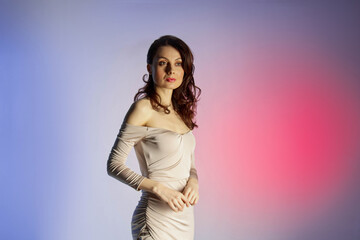 Fototapeta premium Colored background, neon lights, studio shot. Fashion portrait of a young elegant brunette woman in a nice dress.