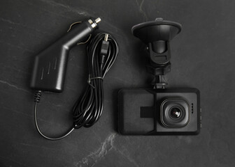 Modern car dashboard camera with suction mount and charger on black background, flat lay