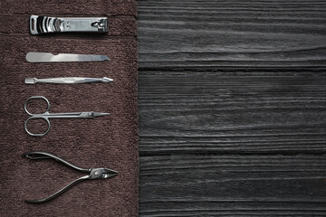 Set of manicure tools and towel on black wooden table, top view. Space for text